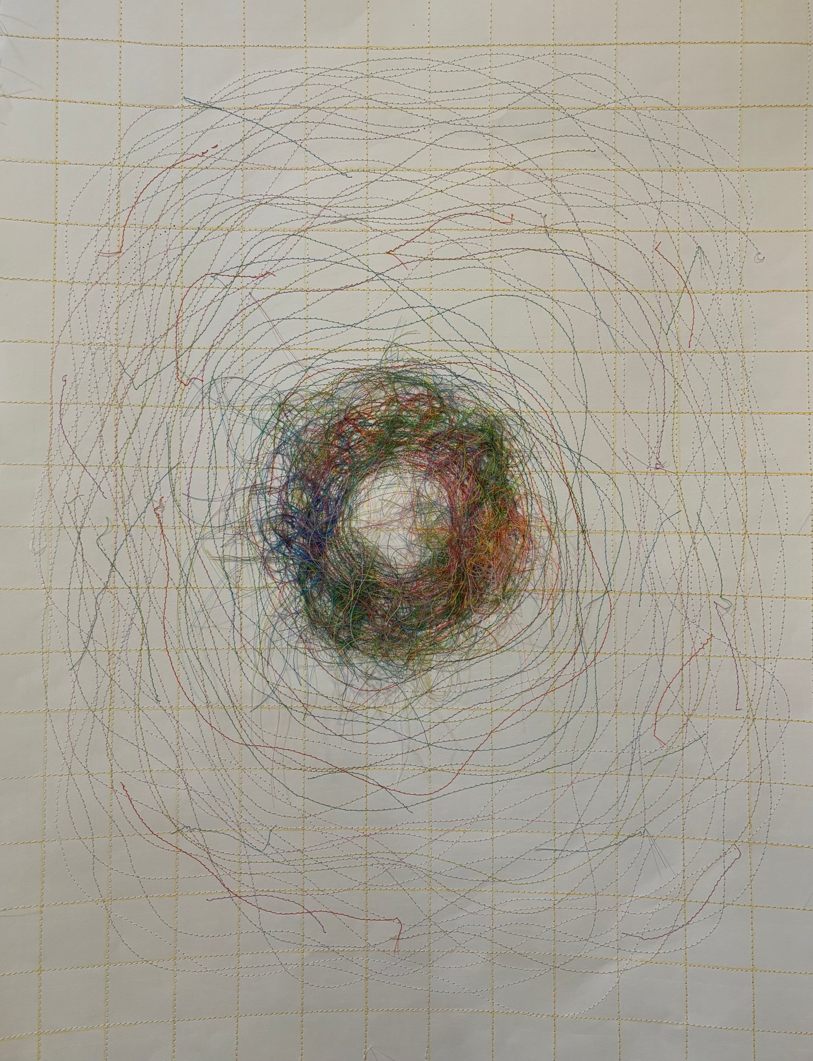 Image is a close-up of an abstract piece sewn on paper, using yellow, blue, purple, pink, and green threads.