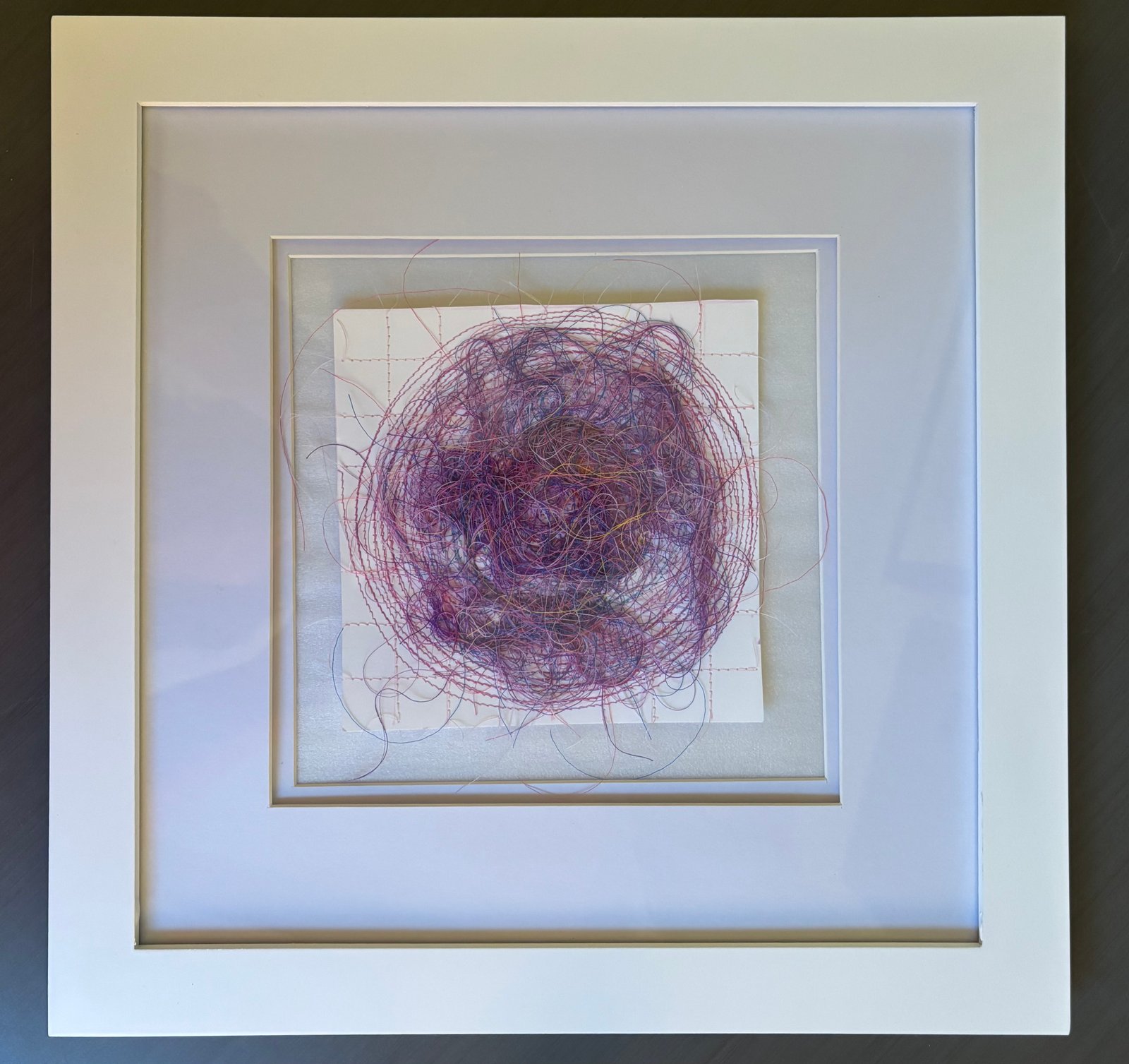 Image is a close-up of an abstract piece sewn on paper, using yellow, blue, purple, pink, and orange threads.