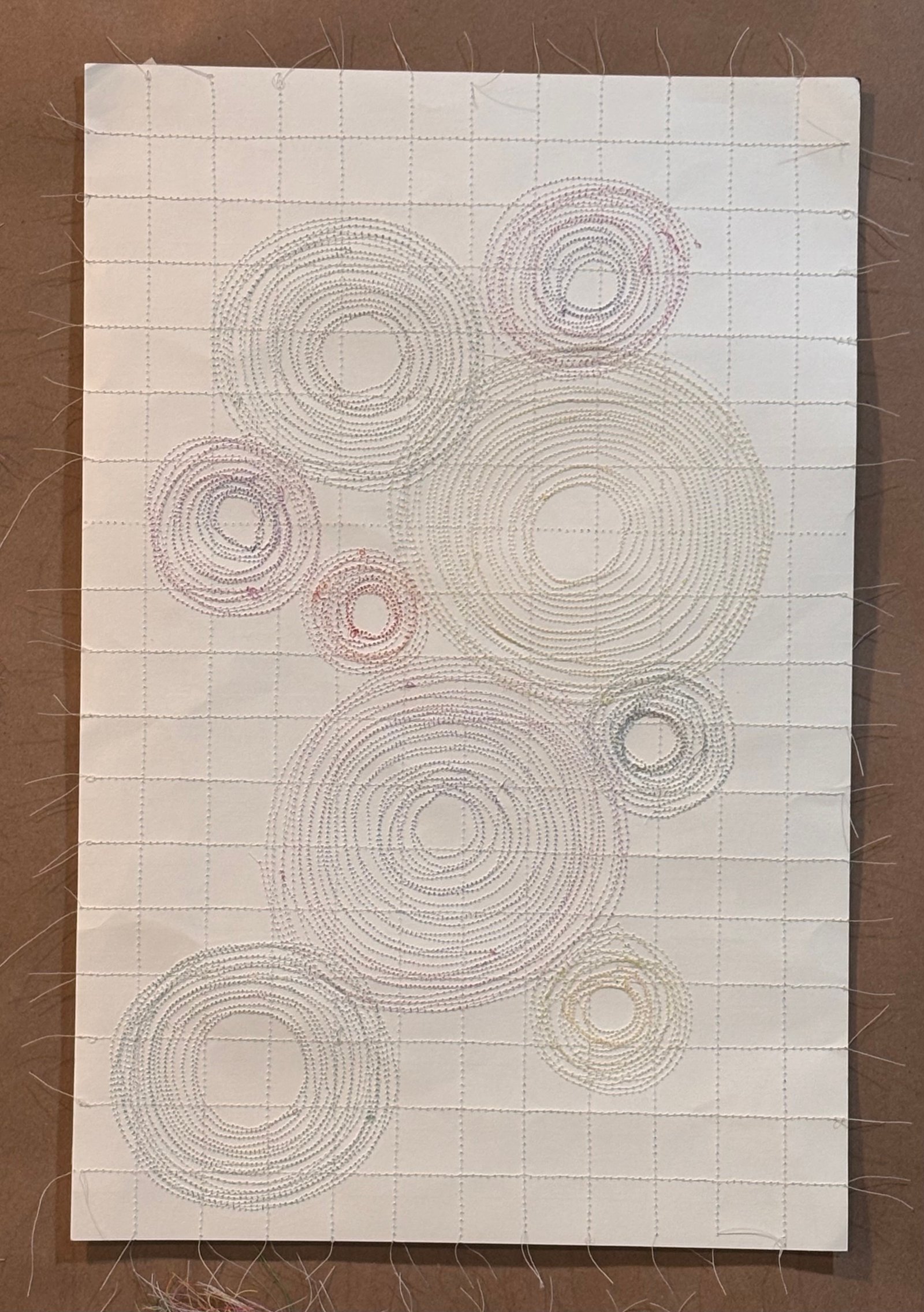 Image is an abstract piece sewn on paper, using orange, green, yellow, blue, and purple color threads.