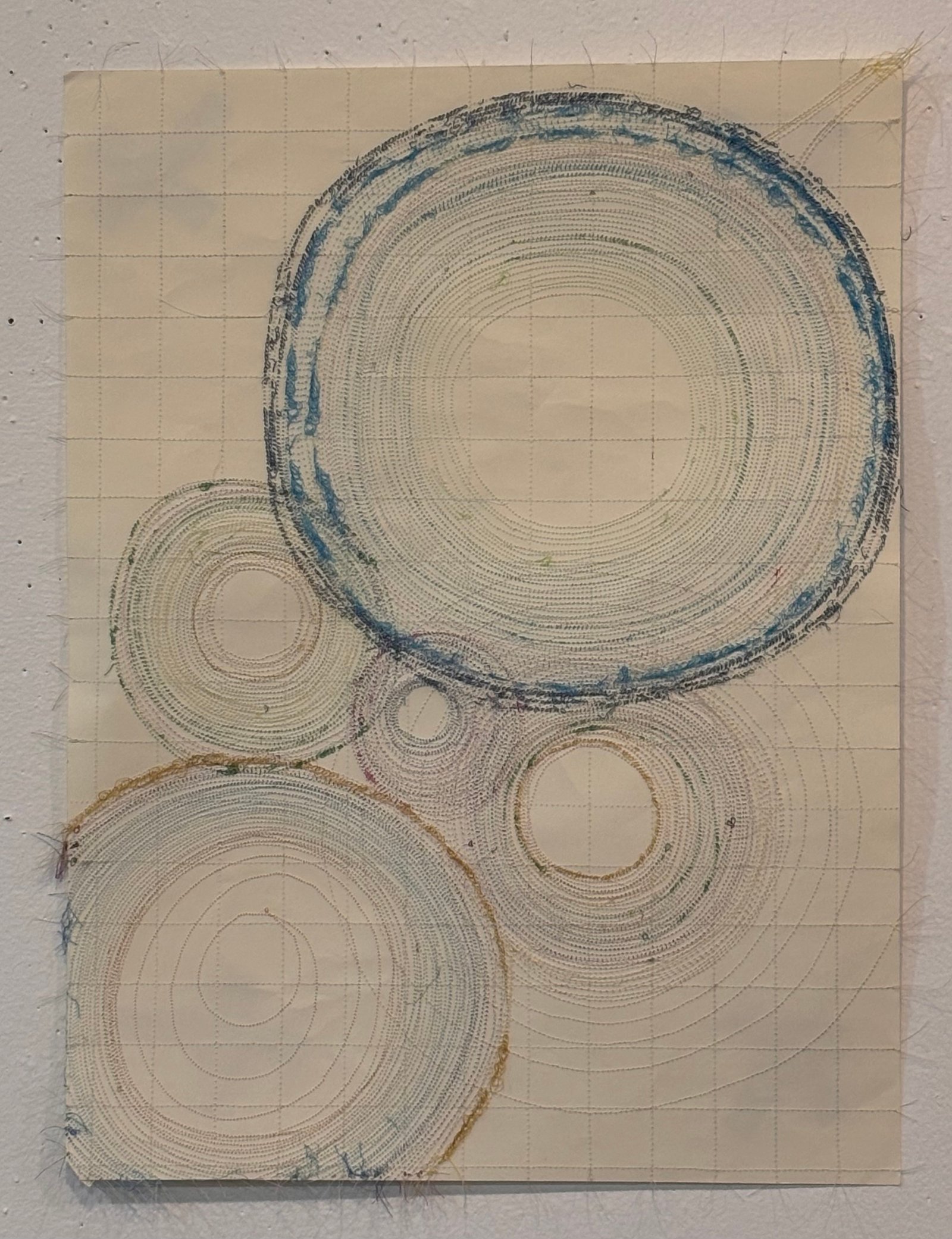 Image is a close-up of an abstract piece sewn on paper, using blue, brown, and purple threads.